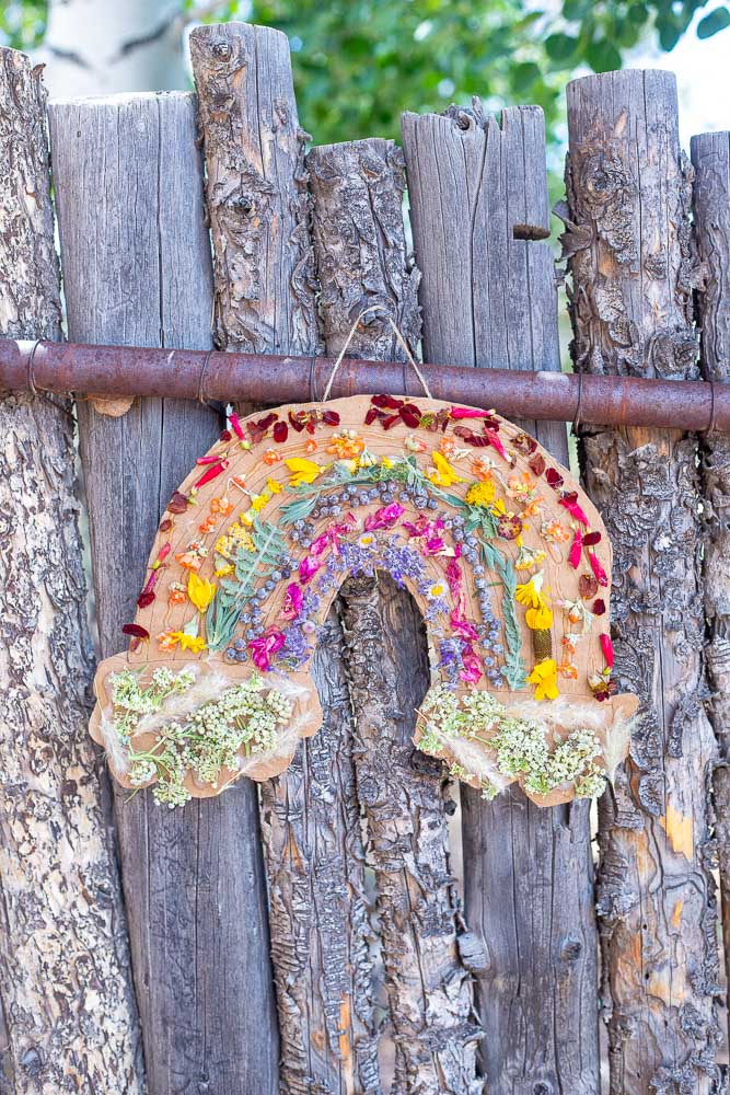Rainbow Flower Wall Hanging hanging on a wooden fence outside